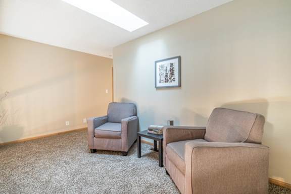 Two chairs and a small table are in a room with a picture on the wall.
