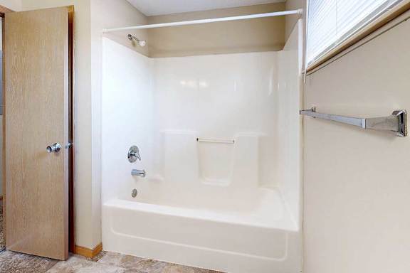 Tub and shower combination with built-in surround, towel bar, and nearby window for natural light.