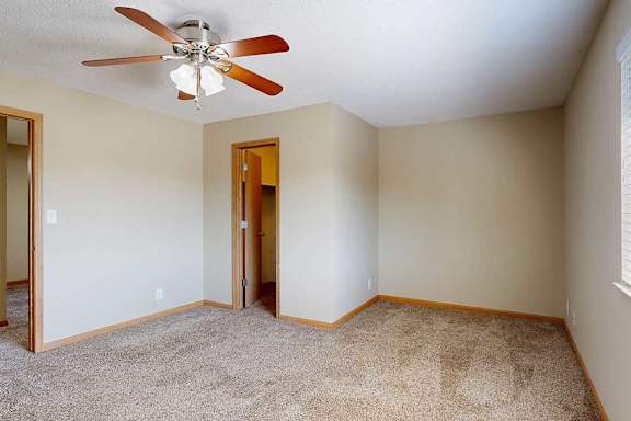 Spacious carpeted bedroom with neutral walls, ceiling fan with light, and doorway access to hallway and walk-in closet.