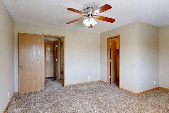 Bright bedroom with plush carpet, ceiling fan, and multiple wood-trim doors leading to closet and main living area.
