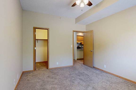 Bedroom with walk-in closet, open doorway to kitchen area, neutral paint, and carpeted floors.