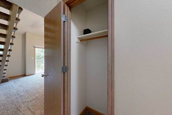 Coat closet with hanging rod and upper shelf, located near the staircase and living area.