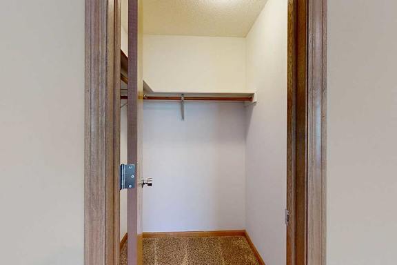 Walk-in closet with carpet flooring, wraparound hanging rods, and upper shelf for organized storage.