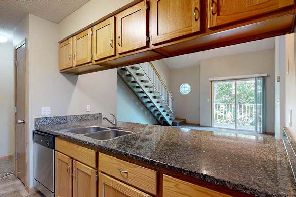 Open kitchen with extended granite-style countertops, double sink, dishwasher, and view of staircase and sliding glass door.