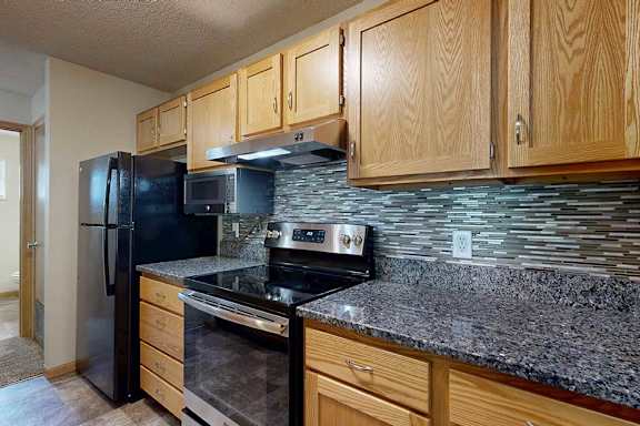 Galley kitchen with wood cabinets, granite-style counters, black appliances, and modern tile backsplash.