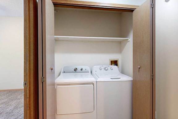 In-unit laundry closet with full-size washer and dryer, overhead shelf, and double doors.