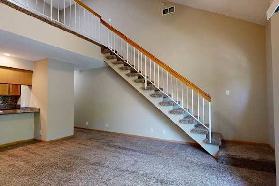 Open living room with carpeted staircase, white railing, and view toward the kitchen and breakfast bar.
