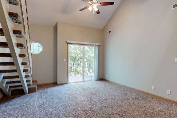 Two-story living area with vaulted ceiling, ceiling fan, sliding glass door to balcony, and open staircase to loft.