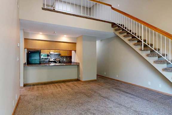 Spacious living room with loft overlook, carpet flooring, and open kitchen with breakfast bar.