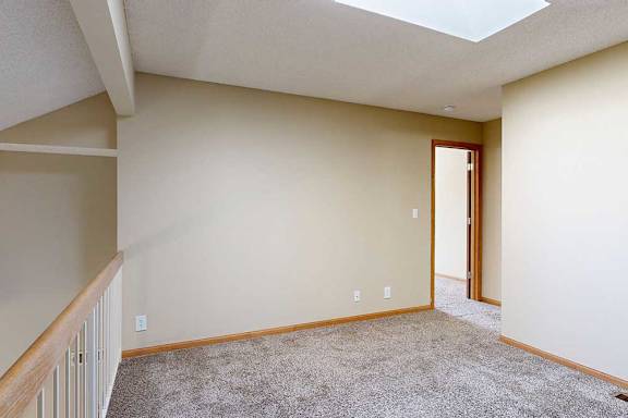 Upper loft area with carpet flooring, white railing, skylight, and view down to the living room below.