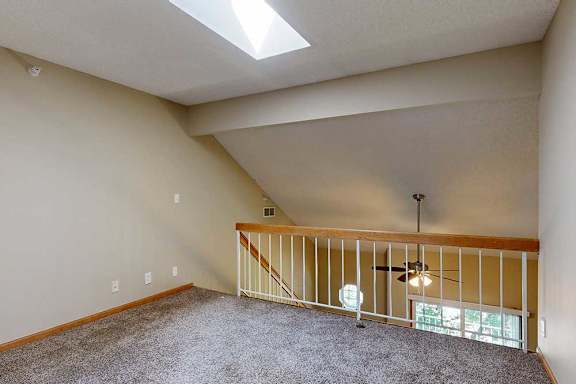 Loft landing with carpet, wood-trim railing, and view of ceiling fan and balcony below.