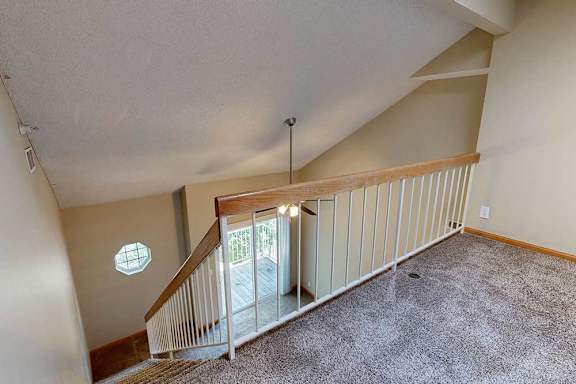 Loft landing with carpet, wood-trim railing, and view of ceiling fan and balcony below.