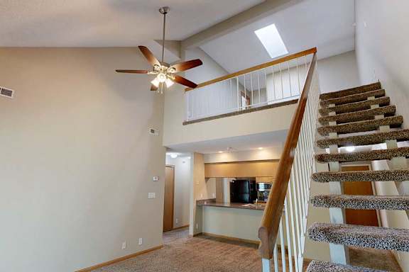 Open staircase with carpeted steps and white railing leading to loft, overlooking the living room and kitchen.