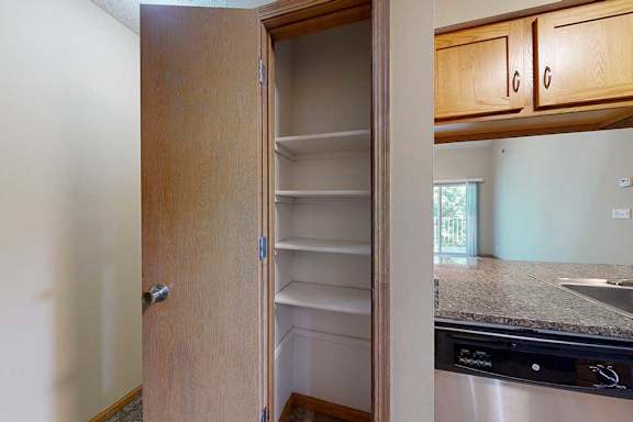 Built-in pantry closet with multiple white shelves, located beside the kitchen with granite-style countertop and dishwasher.