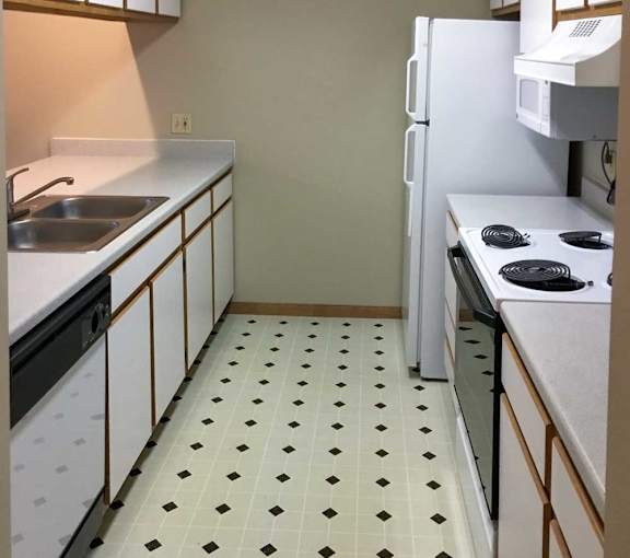 a kitchen with white and brown cabinets, white appliances, and vinyl flooring