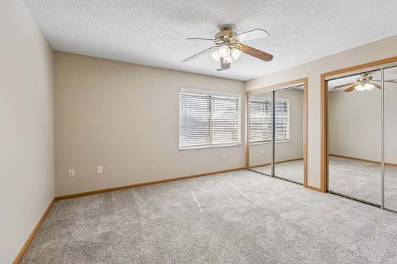 Spacious bedroom with mirrored closet doors, carpet flooring, and ceiling fan.