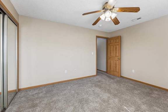 Bright carpeted bedroom with neutral walls, ceiling fan, and wood trim accents.