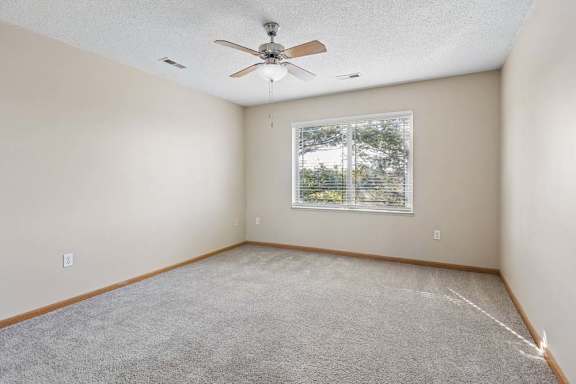 Carpeted bedroom with ceiling fan and window.
