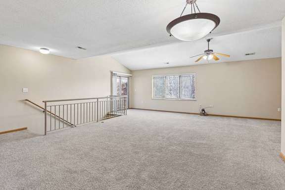Spacious upstairs loft with carpeted floors and stairway railing.