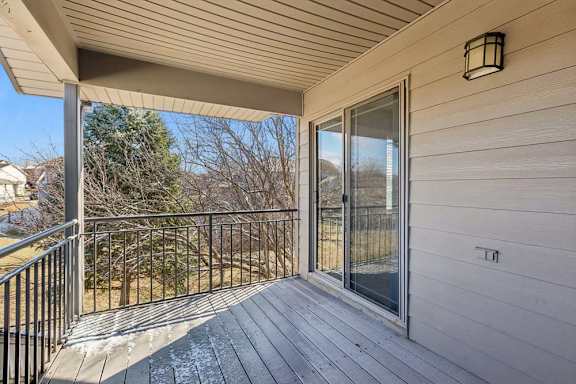 Covered apartment balcony with wood decking, metal railing, and sliding glass door.