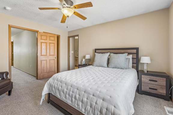 A bedroom with a large bed, a ceiling fan, and a nightstand with a lamp.