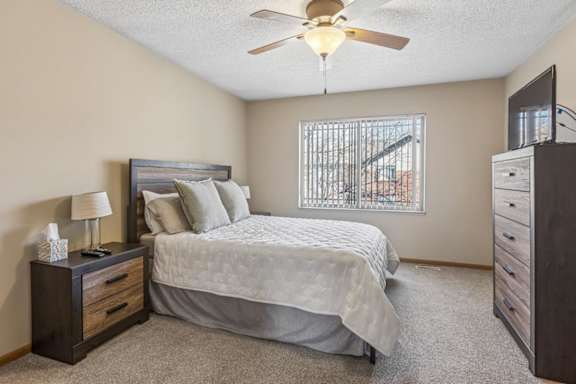 Apartment bedroom with plush carpet, ceiling fan, large window, and neutral finishes throughout.