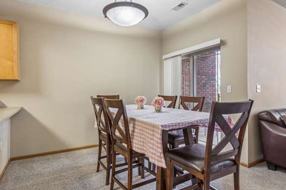 Dining area in an apartment home with table seating, neutral walls, and sliding glass door access nearby.