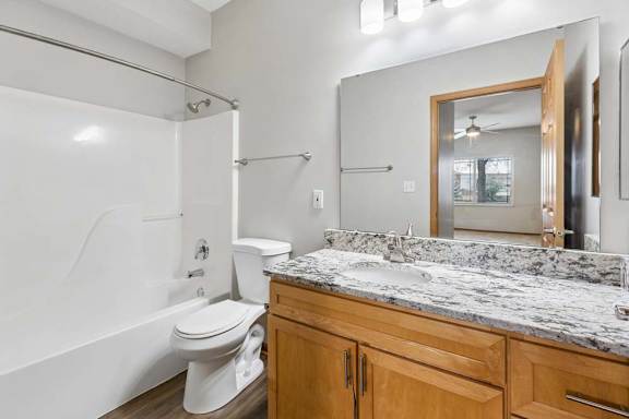 Bathroom featuring granite countertop, large mirror, and tub-shower.