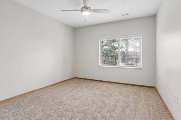 Carpeted bedroom with ceiling fan and window.