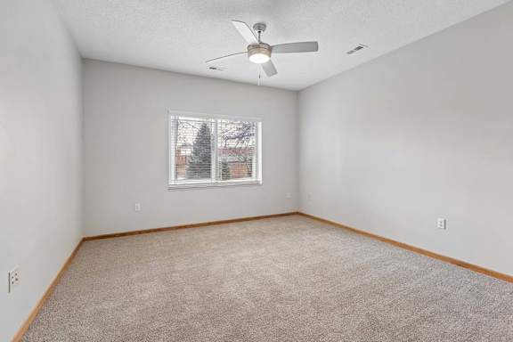 Carpeted bedroom with ceiling fan and window.