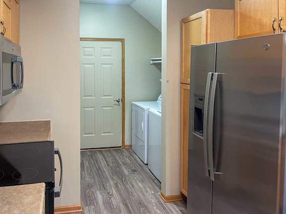 a kitchen with wooden cabinets and stainless steel appliances, with a laundry room in the background
