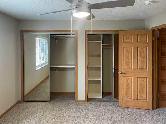 a bedroom with a wooden door, a fan, and two closets with shelves