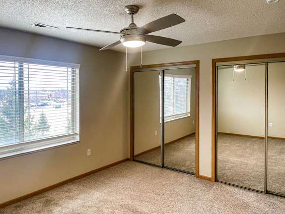 a bedroom with a ceiling fan and two closets with sliding mirrored doors