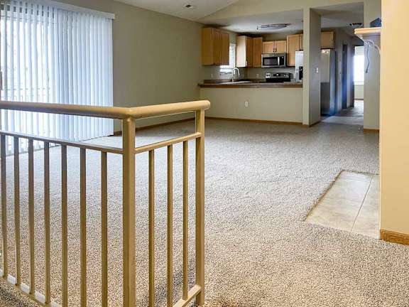 a spacious living area with a carpeted floor and a staircase leading to the entry