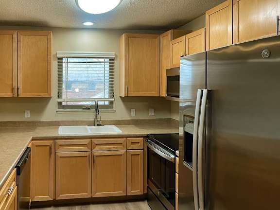 a kitchen with wooden cabinets, stainless steel appliances, and a window above the sink