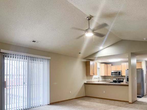 a living room with a sliding glass door to a balcony in front of a kitchen area