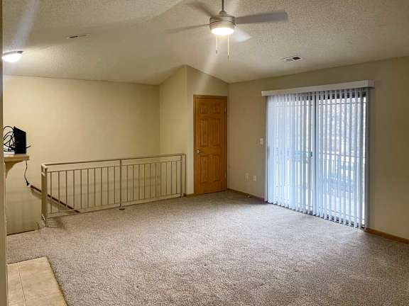 a spacious living room with a ceiling fan, a coat closet, and a sliding glass door to a balcony
