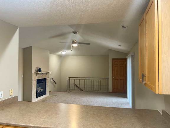 a living room with a fireplace, a ceiling fan, and a metal railing over some stairs
