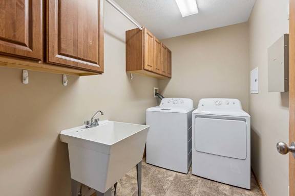Laundry room with washer and dryer, utility sink, wood storage cabinets, tile flooring, and overhead lighting.