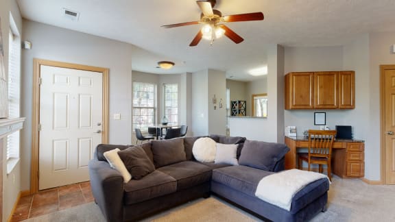 a living room with a large sectional couch and a ceiling fan with built in desk in back