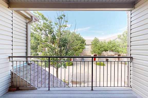 A balcony with a black railing and a view of landscaping and surrounding apartments.