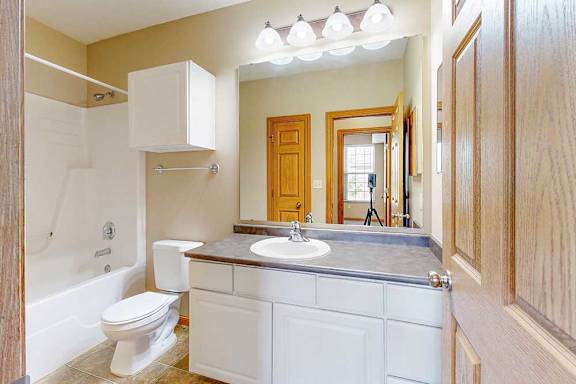 A bathroom with a white cabinets, a large mirror, and a tub shower.