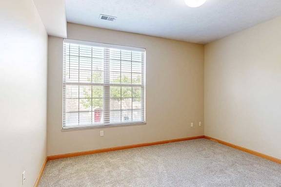 A carpeted bedroom with a large window and blinds.
