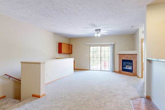 A living room with a fireplace, a sliding glass door, and a half wall around the stairs to the private entry.
