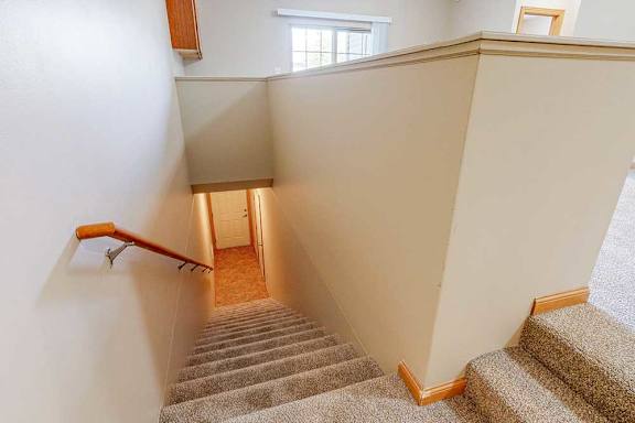A carpeted staircase leading up from a private entry and door to an attached garage, with a wooden handrail.