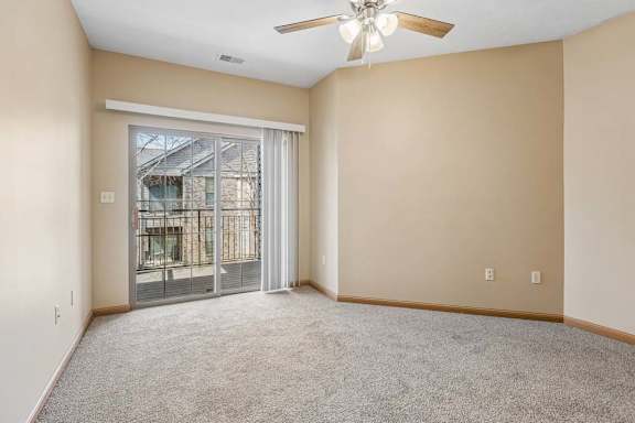 Bright apartment bedroom with neutral carpeting, a ceiling fan, and sliding glass doors opening to a private balcony.