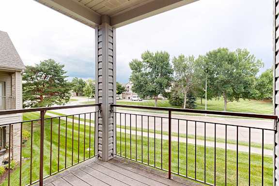 A balcony with a metal railing and a view of a grassy area and trees.