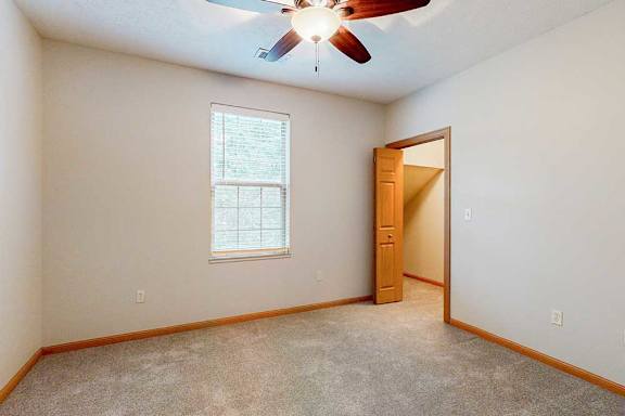 A bedroom with a walk-in closet, a ceiling fan, and a window.