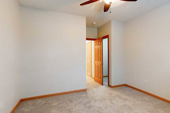 A bedroom with a carpeted floor, a ceiling fan, and a walk-in closet.