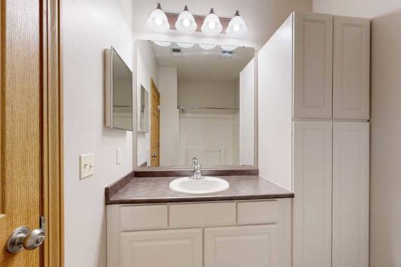 A bathroom with a vanity sink, mirror, medicine cabinet, and tall storage cabinet.